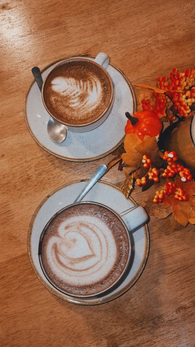 Two coffees with latte art on a wooden table styled with autumn berries and leaves