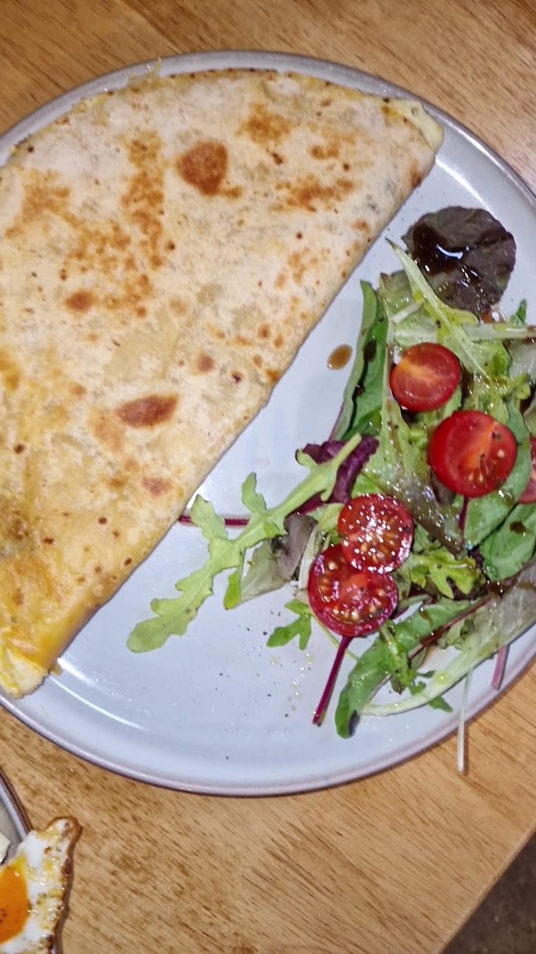 A folded quesadilla on a plate with a dressed side salad