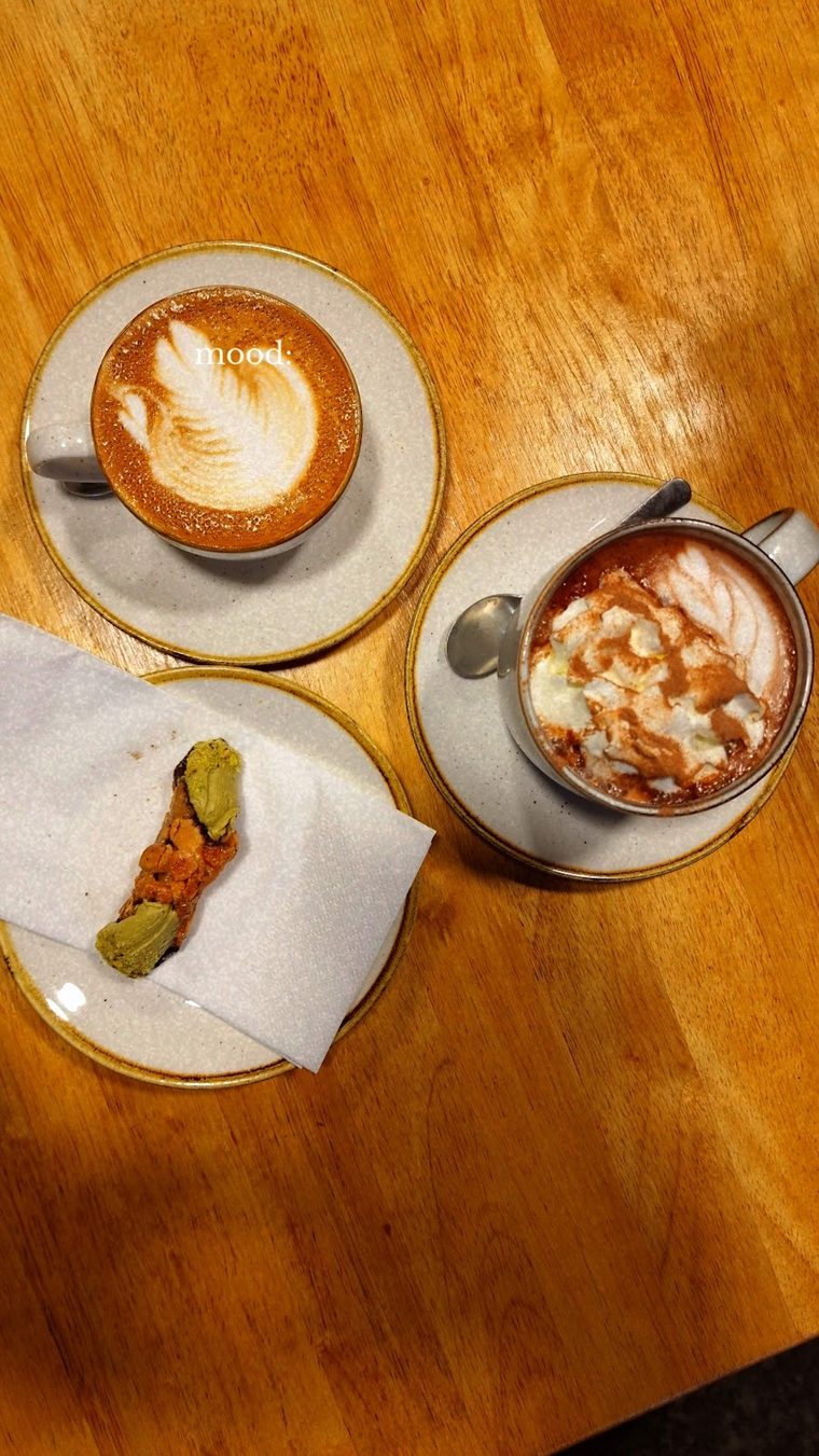 A hot chocolate topped with marshmallows beside a latte and a small biscuit
