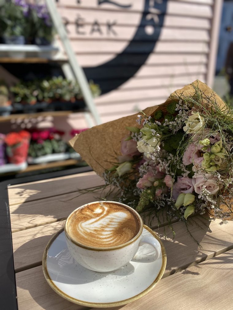 A latte with rosetta art on an outdoor table beside a wrapped bouquet